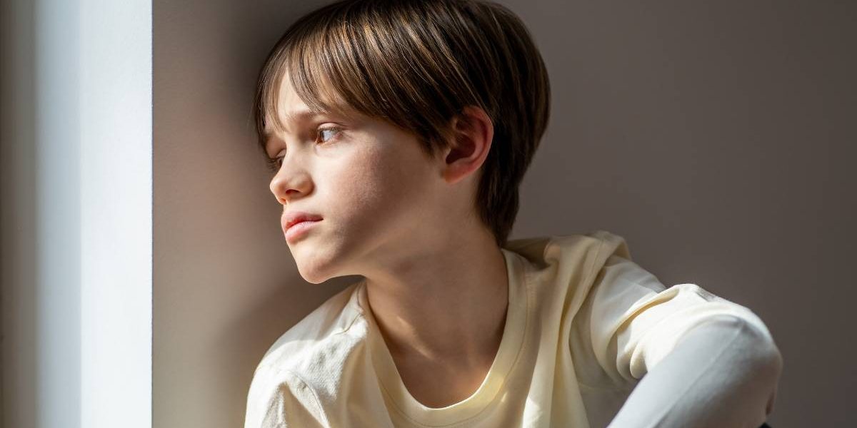a kid is sitting on the floor looking out the window.