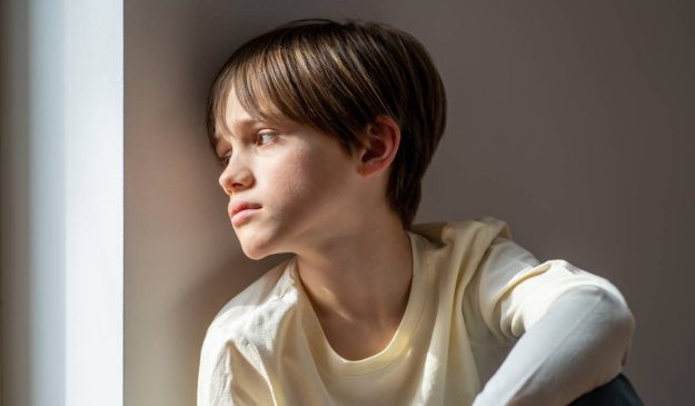 a kid is sitting on the floor looking out the window.