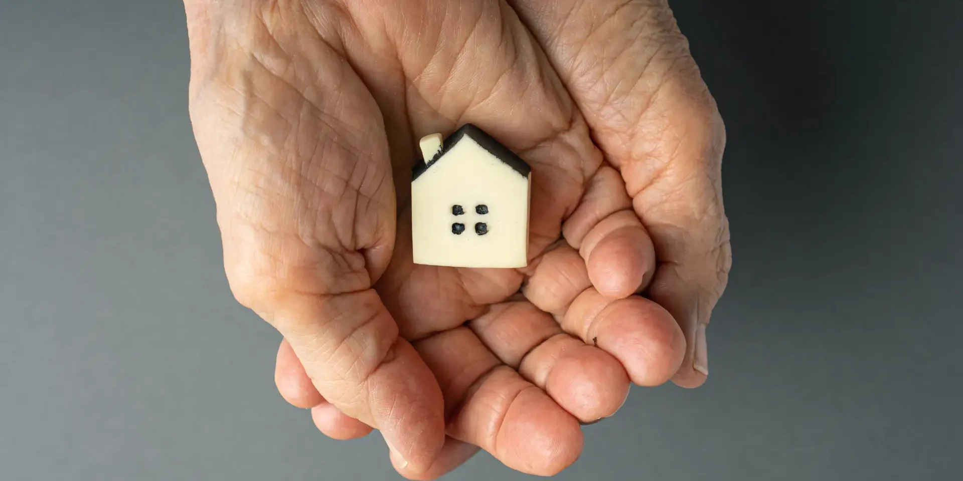 an elderly person holding a small house in their hands