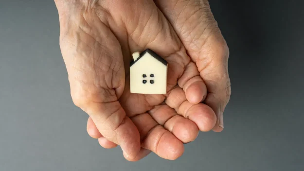 an elderly person holding a small house in their hands