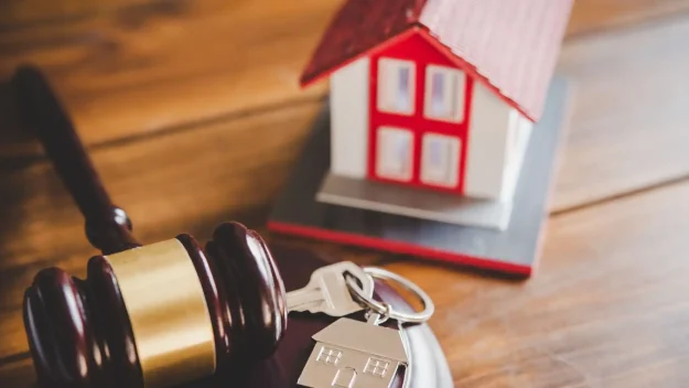 a judge's gavel, house keys, and a model of a house on a wooden table
