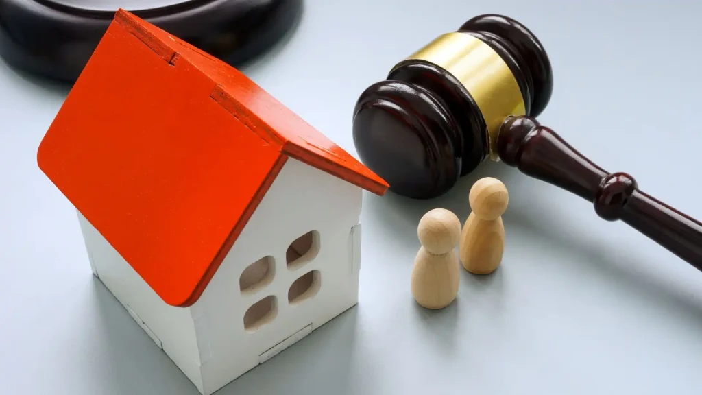 a judge's gavel next to a model house and wooden blocks on a gray background