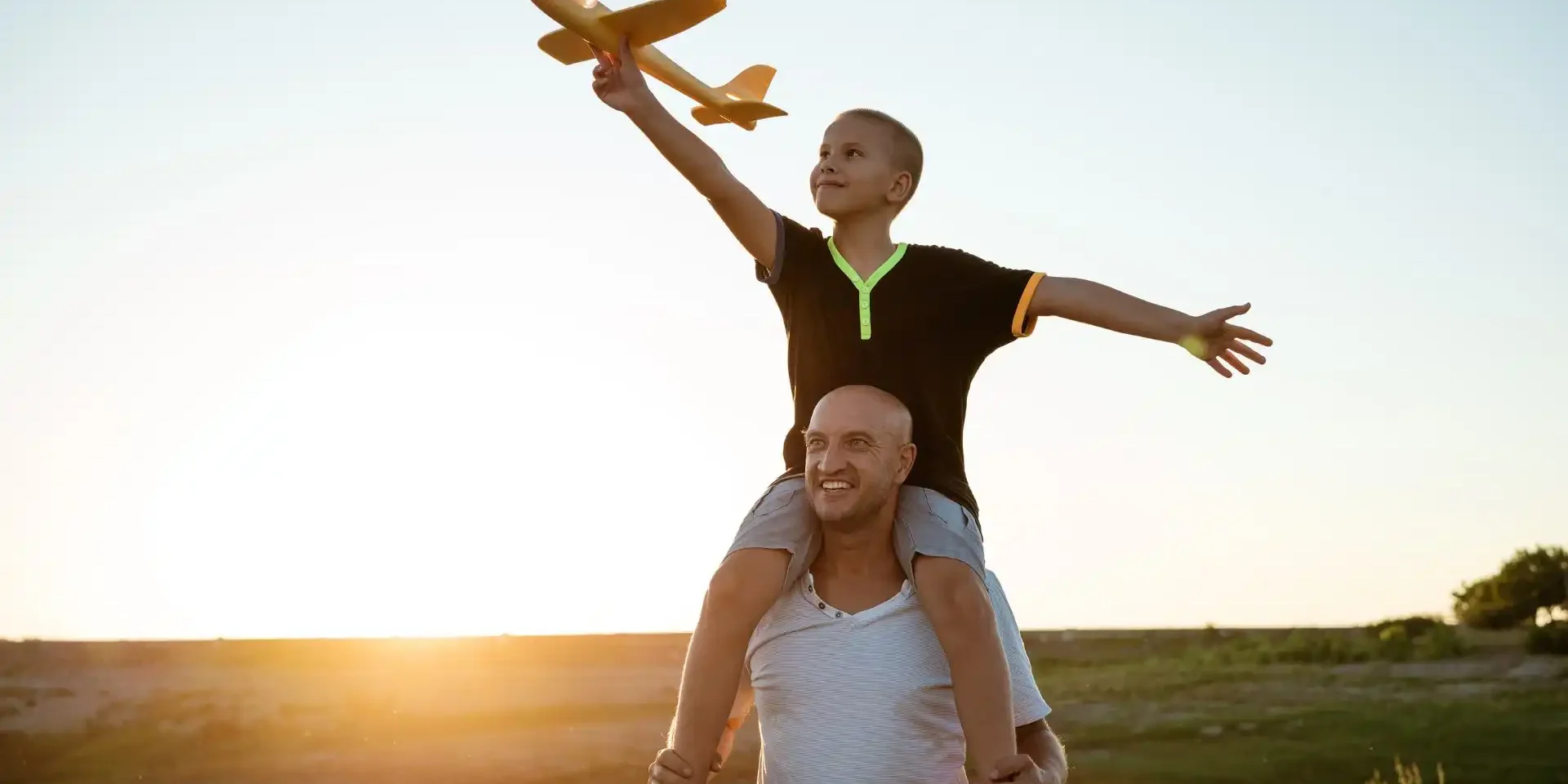 A parent and child playing with a toy plane at sunset