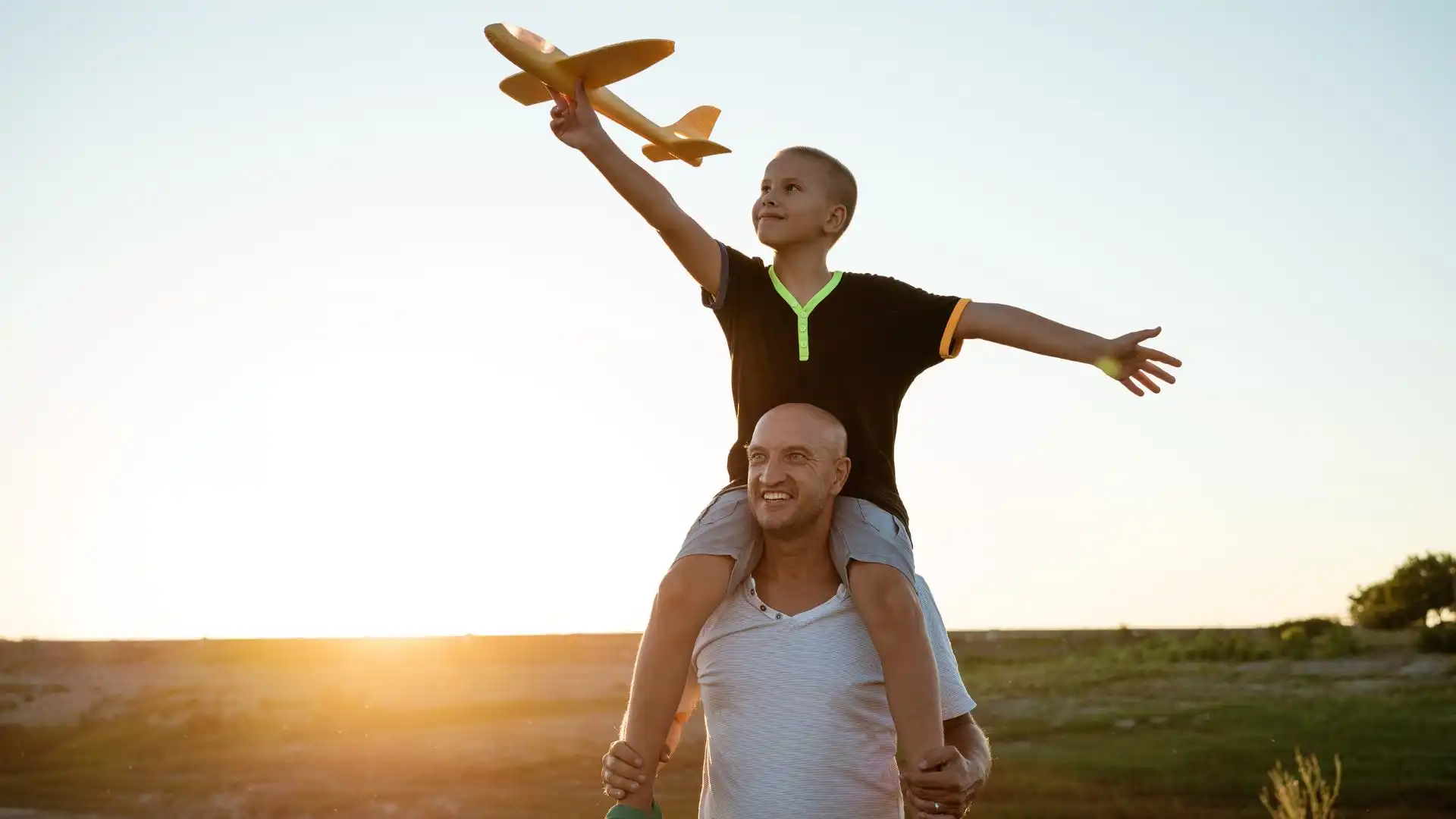 A parent and child playing with a toy plane at sunset