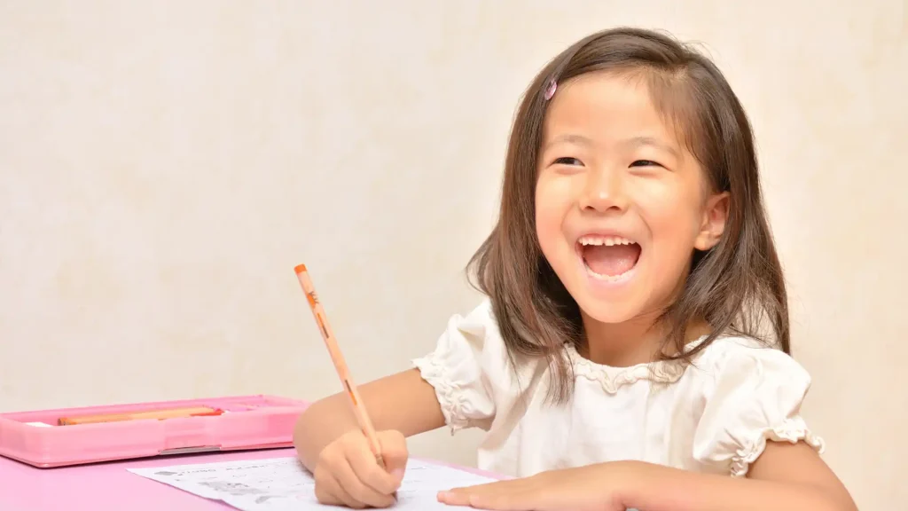 a child smiling while writing on a paper.