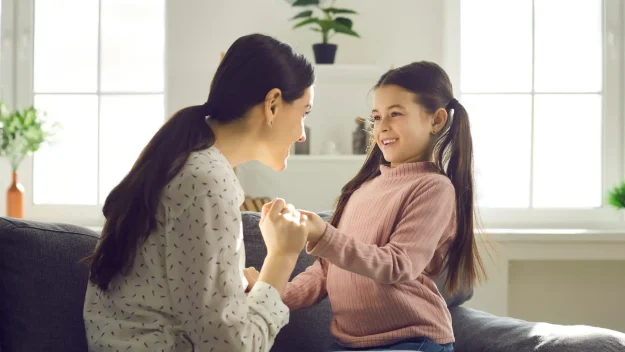 Mother holding daughter's hand while smiling and talk about adoption