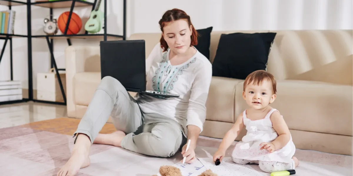 a woman is working on her laptop next to her child in front of a couch