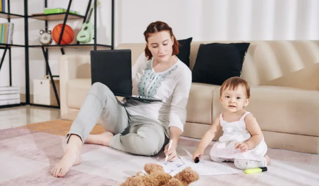 a woman is working on her laptop next to her child in front of a couch