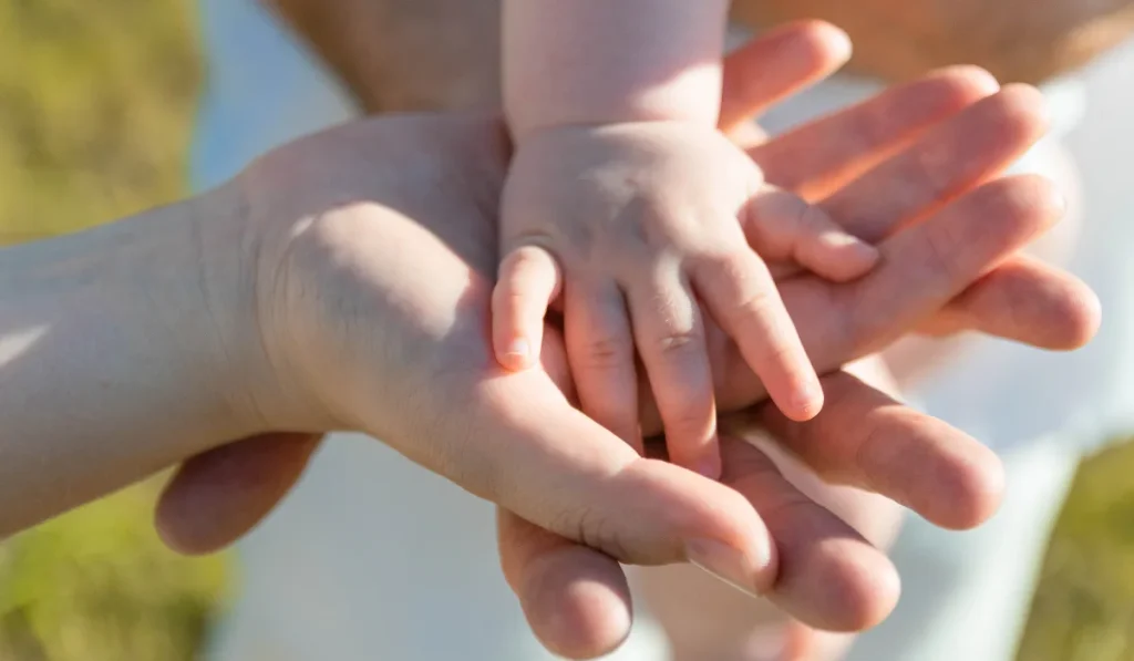 A child’s hand resting on top of their parents’ hands, symbolizing love and support.