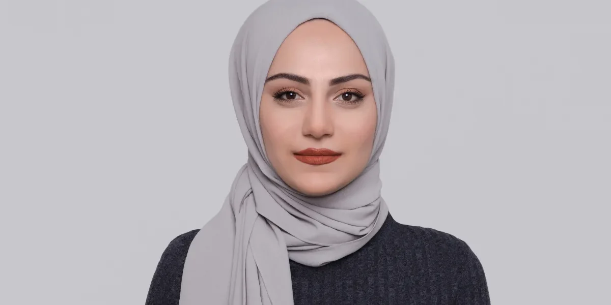 Woman wearing a grey hijab against a plain background